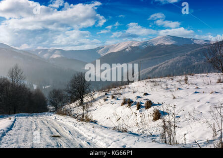 Ländliche Straße in der verschneiten Berglandschaft. schöne Winterlandschaft auf einem hellen, sonnigen Tag. Berge mit schneebedeckten Gipfel in der Ferne Stockfoto