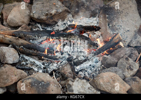 Glühende heiße Kohle auf einem Holzfeuer umgeben von kleinen Felsen oder Steinen auf einem Campingplatz aus nächster Nähe Stockfoto