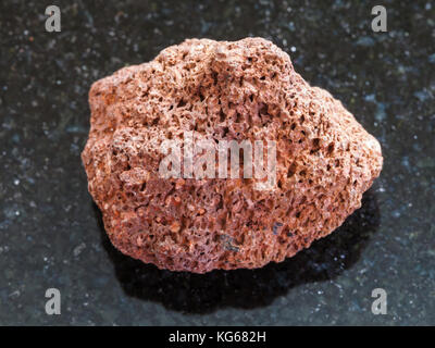 Makroaufnahmen von natürlichen Mineralgestein Muster - trommelsteine rot Bimsstein auf dunklem Granit Hintergrund aus Sizilien Stockfoto