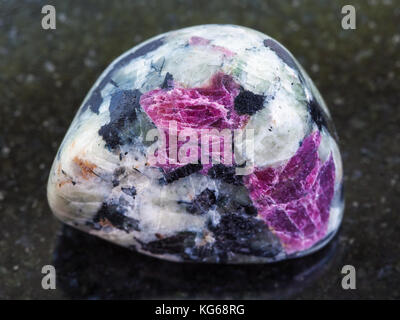Makroaufnahmen von natürlichen Mineral Stein Muster - trommelsteine rosa Korund Kristalle in Rock auf dunklem Granit Hintergrund Stockfoto