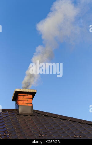 Rauch aus gemauerten Schornstein auf dem Dach gegen den blauen Himmel Stockfoto