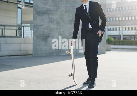 Eine moderne Geschäftsmann auf der Straße stand und halten ein Skateboard. Stockfoto