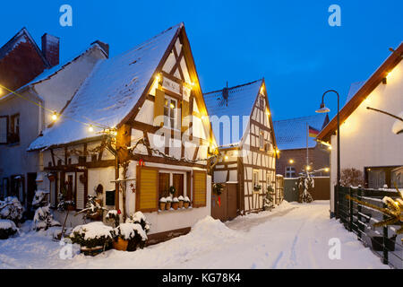 Eine alte Dorfstraße mit Fachwerkhäusern und Weihnachten Lichter in der Nacht bei Schneefall in Haines, Edenkoben, Deutschland. Stockfoto