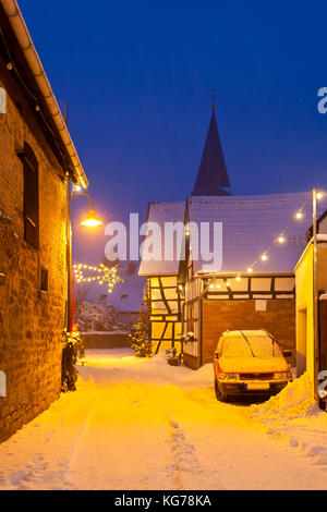 Eine alte Straße mit Fachwerkhäusern und Weihnachten Lichter in der Nacht bei Schneefall in Haines, Edenkoben, Deutschland. Stockfoto