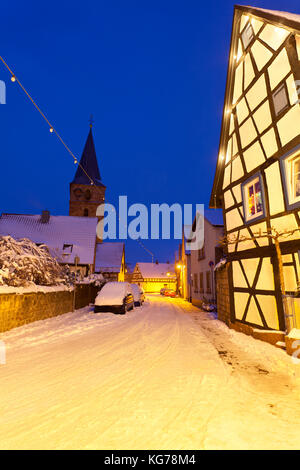 Eine alte Straße mit Fachwerkhäusern und Weihnachten Lichter in der Nacht bei Schneefall in Haines, Edenkoben, Deutschland. Stockfoto