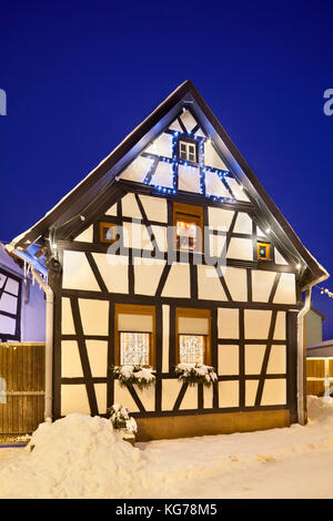 Eine Gasse mit Fachwerkhäusern und Weihnachten Lichter in der Nacht bei Schneefall in Haines, Edenkoben, Deutschland. Stockfoto