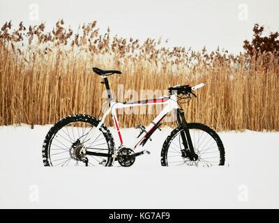 Das Mountainbike Aufenthalt im Schnee. verloren weg in tiefe Schneeverwehungen. Schnee schmilzt auf dunklen off road Reifen. Winter in das Feld ein. Stockfoto