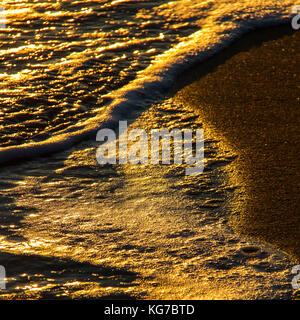 Nahaufnahme der abstrakten bunte Formen durch brechende Wellen auf einem Sandstrand und Sonne Reflexionen bei Sonnenuntergang erstellt Stockfoto