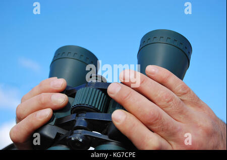 Fernglas in der Hand eines Mannes in den blauen Himmel auf der Suche Stockfoto