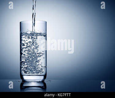 Gießen Sie Wasser in Glas mit Reflexion auf Blau grauer Hintergrund Stockfoto