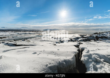 Winterlandschaft, Risse im Schnee bedeckten Boden mit der Sonne am blauen Himmel, in pingvellir Nationalpark in Island Stockfoto