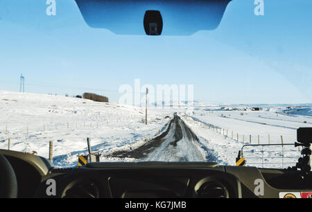 Die Fahrt auf der Landstraße im Winter. Durch auto Frontscheibe suchen, gefrorene Straße mit Schnee bedeckt und strahlend blauer Himmel in Island Stockfoto