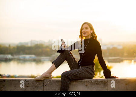 Trendige junge Frau hört Musik von Smartphone outdoor bei Sonnenuntergang Stockfoto