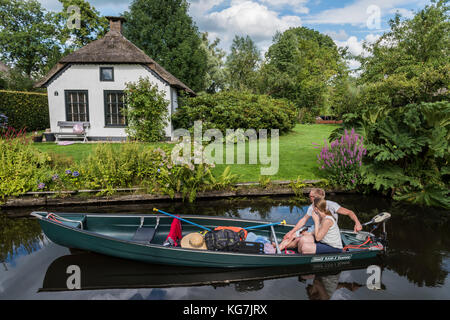 Giethoorn, Niederlande - 30. Juli 2016: Elektroboot mit tw Menschen vor einer monumentalen Haus in dem kleinen, malerischen Städtchen Giethoorn, Stockfoto