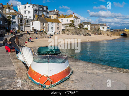 St. Ives, England - 27. April 2017: Touristen in der Sonne sitzen am Kai auf den Hafen von St. Ives mit Boote, klares Wasser, Strand und Häuser. Stockfoto