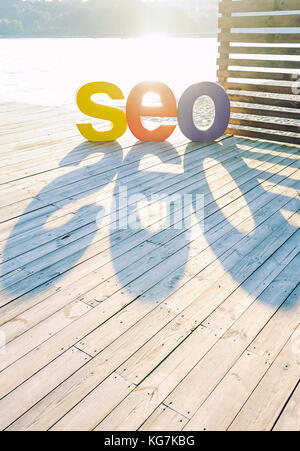 Das Wort seo von großen farbigen Buchstaben erstellen einen Schatten auf der hölzernen Terrasse am Ufer. sun Hintergrundbeleuchtung. Selektive konzentrieren. Platz für Text. Stockfoto