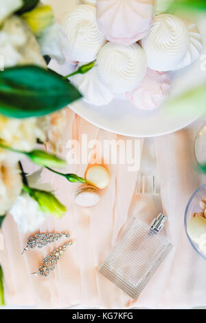 Bridal morgen details Zusammensetzung. nach oben Blick auf die Braut Schmuck, Parfums, Blumenstrauß aus eustoma Blumen und Eibisch und Makronen Süßigkeiten. Flach. Stockfoto