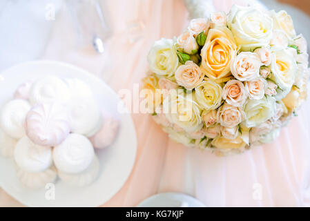 Hochzeit Details. nach oben Blick auf die Braut Blumenstrauß aus Licht Rosen Blumen auf dem Tisch mit Parfums und arshmallow Süßigkeiten. Flach. Selektive konzentrieren. Raum Stockfoto