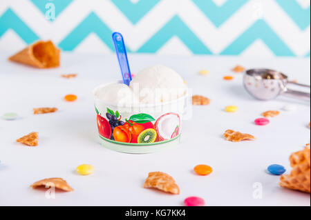 Bis Vanille Eis in einem Pappbecher auf dem weißen Hintergrund mit bunten Bonbons schließen, Waffeln, Eis Löffel und leeren Eis. Stockfoto