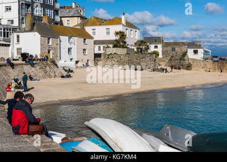 St. Ives, England - 27. April 2017: Touristen in der Sonne sitzen am Kai auf den Hafen von St. Ives mit Boote, klares Wasser, Strand und Häuser. Stockfoto