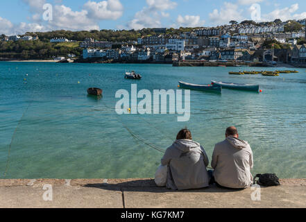 St. Ives, England - 27. April 2017: Touristen in der Sonne sitzen am Kai auf den Hafen von St. Ives mit Boote, klares Wasser und Häuser. Stockfoto