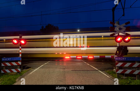 Woudenberg, Niederlande - 21 August 2017: Gelb und Blau ns-Zug mit Lichtern, vorbei an einem Bahnübergang in der Nacht in den Niederlanden. Stockfoto