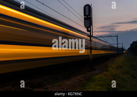 Woudenberg, Niederlande - 21. August 2017: Gelber und blauer NS-Zug mit Lichtern, die nachts in den Niederlanden vorbeifahren. Stockfoto