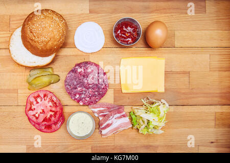 Zutaten zum Kochen Burger. rohes Hackfleisch Fleisch Schnitzel, Zwiebeln, Tomaten, Salat, Gurken, Saucen, Käse, Ei und Speck auf den hölzernen Häckseln Stockfoto