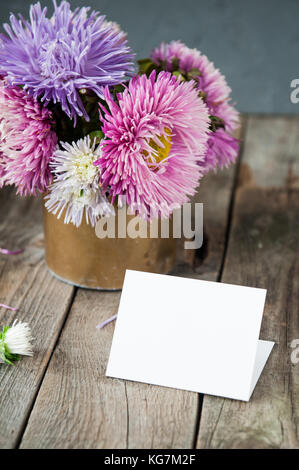 Multicolor aster Blumen Blumenstrauß, leere weiße Grußkarte auf rustikalen Holztisch und dunkelgrauem Hintergrund. Postkarte mock up. Herbst Blumen. selecti Stockfoto