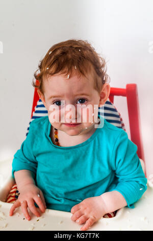Baby, lustig beleidigt Gesicht in den Hochstuhl mit Reis alle über den Kopf - Entwicklung Konzept verwechselt Stockfoto