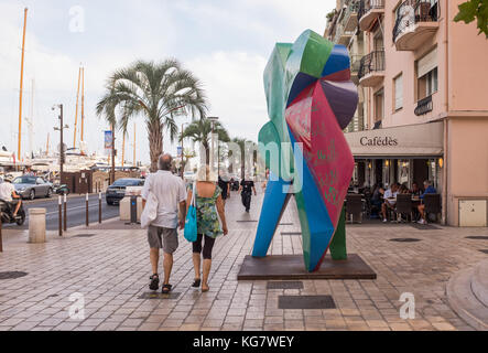 Touristen, die auf dem Bürgersteig in der Nähe von bunten Skulpturen in Quai Saint Pierre, Cannes, Cote d'Azur, Provence-Alpes-Cote d'Azur, Frankreich. Stockfoto