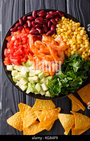 Salat mit Garnelen und Gemüse und Nachos close-up auf dem Tisch. Senkrechte Draufsicht von oben Stockfoto