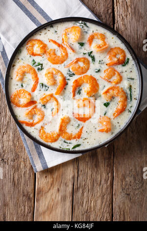 Garnelen mit Spinat und Parmesan in Sahnesoße close-up auf einem Teller auf dem Tisch. Senkrechte Draufsicht von oben Stockfoto