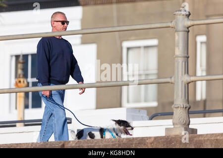 Ein Mann, der seinen Hund an der Hastings Strandpromenade an einem hellen und sonnigen Wintern morgen, Hastings, East Sussex, Großbritannien Stockfoto