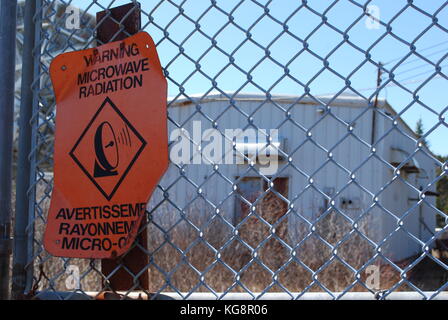 Mikrowelle Strahlung Warnzeichen zu einem Maschendrahtzaun, außerhalb einer verlassenen Radar anlage, Bay Bulls, Newfoundland Labrador, Kanada. Stockfoto