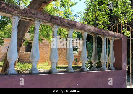 Rosa Zement halbe Wand mit rosa Geländer und dekorative weiße Baluster, Varadero, Kuba. Weiße Tor, tropischen Bäumen und cinder Blockstruktur verrostet. Stockfoto