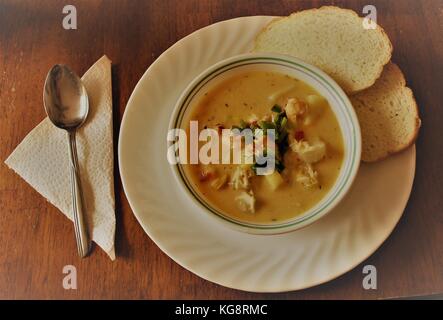 Hausgemachte Meeresfrüchte-eintopf mit selbstgebackenem Brot, in einer weißen Schüssel serviert, auf einer weißen Platte, auf einem Holztisch. Stockfoto