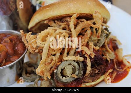 Zog pork Sandwich mit frittierten Zwiebeln und Jalapenopfeffer, und eine Seite von Baked Beans, auf einem Bürgersteig Tabelle in Key West, Florida, USA. Stockfoto