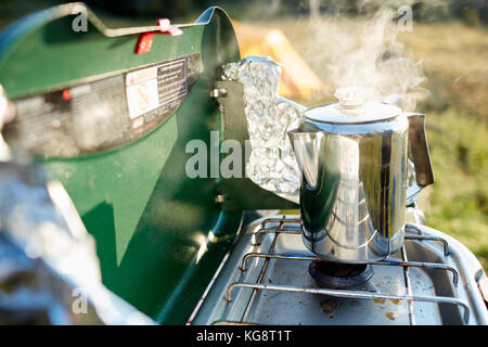 Heizung Wasser für Kaffee auf einem Gasbrenner in einem dampfenden Edelstahl Topf beim Camping im Freien Stockfoto