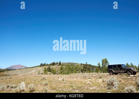 4WD-Fahrzeug durch die malerische Berge fährt auf einem schmalen Feldweg entlang einer grasbewachsenen Grat unter einem sonnigen blauen Himmel Stockfoto