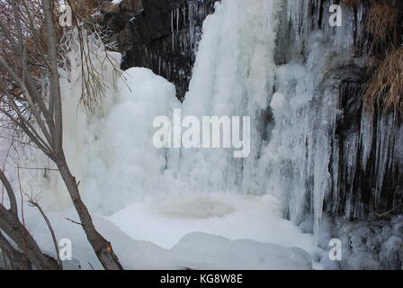 Wasser aus einem Wasserfall einfrieren auf den Felsen, und auf dem Boden, die Schaffung einer Kuppel aus Eis mit einem Pool von Wasser in der Mitte. Stockfoto