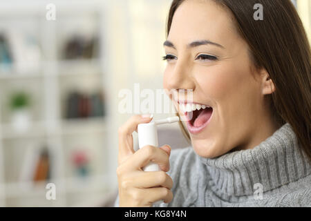 Glückliche Frau tragen Jersey mit einem analgetikum Spray die Kehle sitzt auf einem Sofa in einem Haus innen weich zu machen Stockfoto