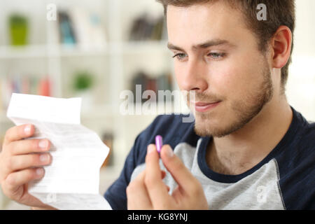 Mann Lesen einer Packungsbeilage vor eine rosa Pille sitzt auf einem Sofa im Wohnzimmer in einem Haus innen zu nehmen Stockfoto