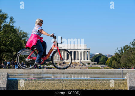 Weibliche Radfahrer reiten ein Kapital Bikeshare Fahrrad mit der Abraham Lincoln Memorial im Hintergrund, Washington, DC, Vereinigte Staaten von Amerika, USA. Stockfoto