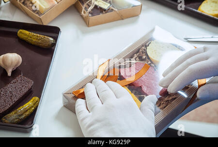 Close-up Packer mit sterilen weißen Handschuhe Packs Eine Reihe von Schokolade aus Vollmilch Schokolade in Form von Wurst, Käse und Brot für ein Geschenk für den ne Stockfoto