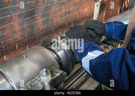 Nahaufnahme eines Monteur in einer blauen Uniform arbeiten an auf einer automatischen Schweißanlage für die Reparatur. Der Mann arbeitet in der Fabrik bei der Instandsetzung von Gelenkwellen Stockfoto