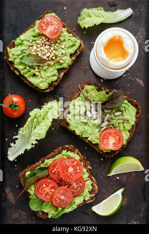 Gesunden grünen veggie Toast mit Avocado, Tomaten, Sprossen und Samen und gekochtem Ei auf Rusty Hintergrund. Tabelle Ansicht von oben. Gesunde Lebensmittel, vegane Ernährung anhand von quantitativen Simulatio Stockfoto