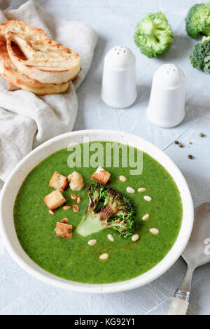 Broccoli creme Suppe mit Croutons und gerösteten Pinienkernen in Weiß Schüssel auf hellen blauen Tisch. gesunden grünen Essen, Diäten, gesunden Lebensstil Konzept Stockfoto