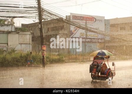 Dreirad und ein Passant bei einem schweren Sturm in Cagayan de Oro, Mindanao, Philippinen. Stockfoto