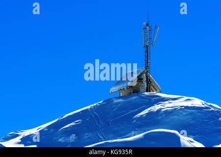 Kleines Holzhaus mit Kommunikationsantennen auf einem schneebedeckten Berg Stockfoto